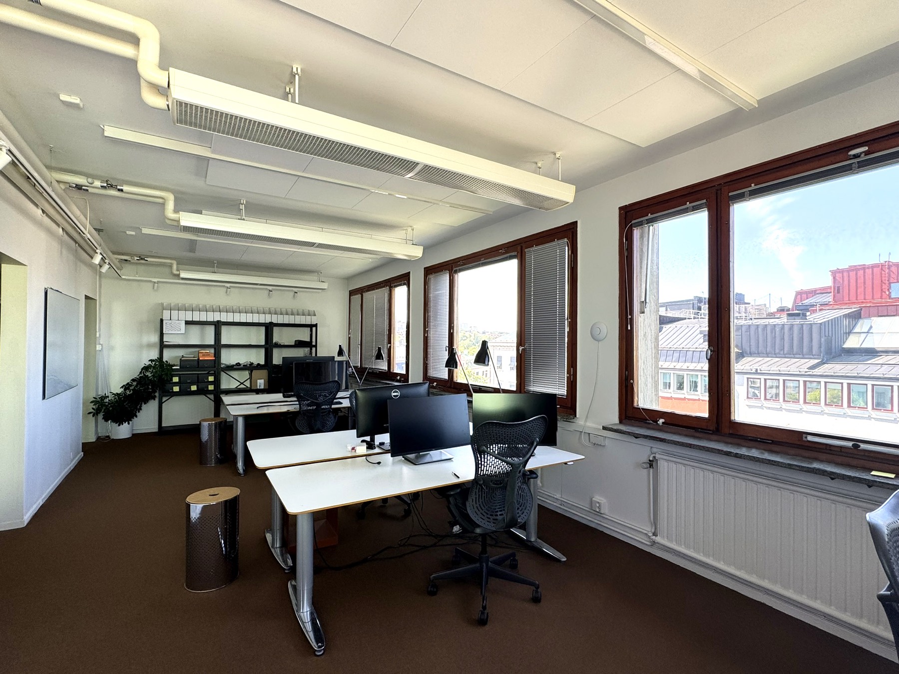 Arbetsrum med skrivbord, hyllsystem och fönster mot innergård.