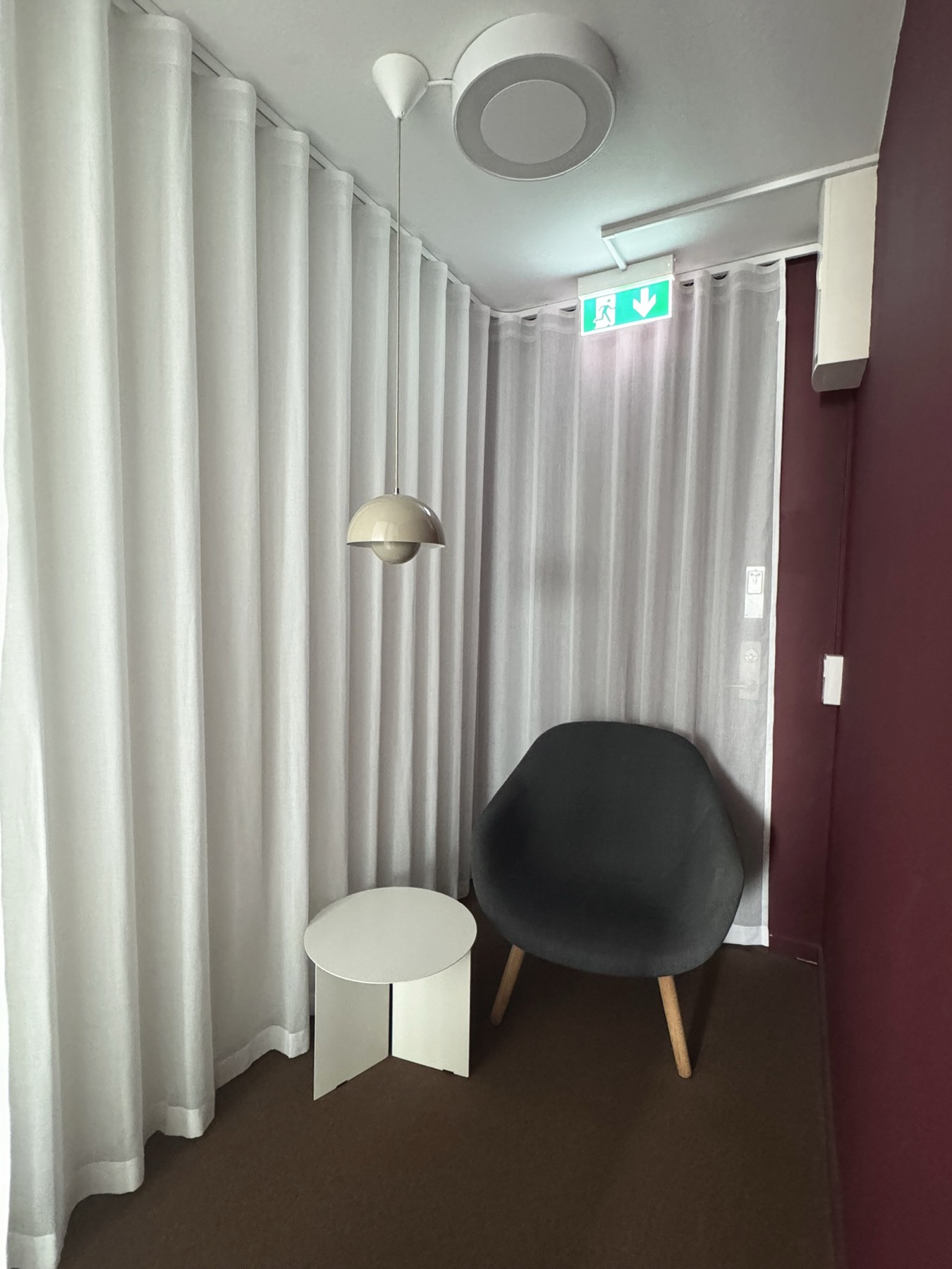 Litet tyst rum med fåtölj, sidobord och draperier.